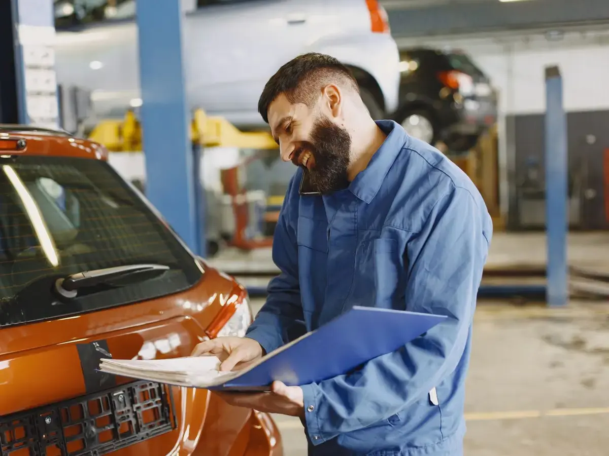 A smiling mechanic talking with a customer beside a car.