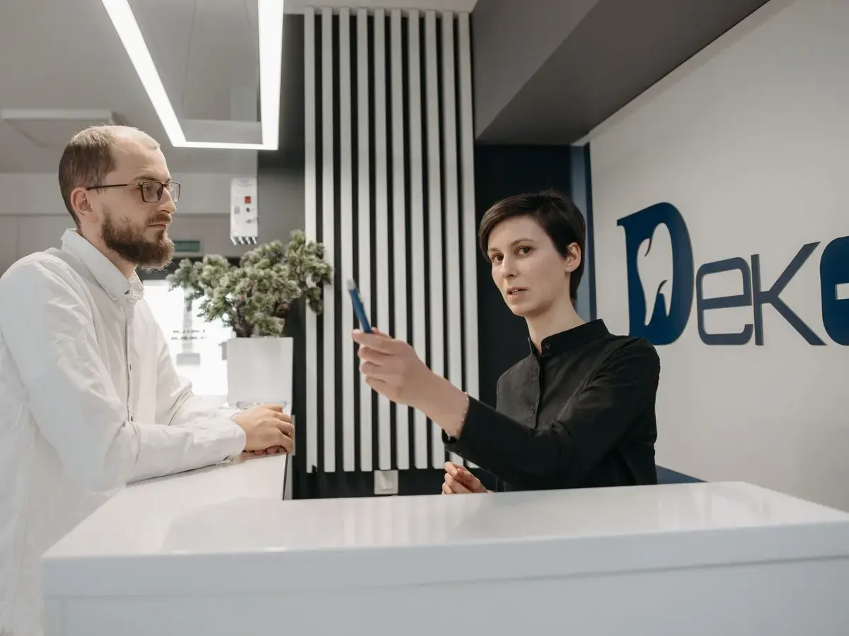 A receptionist welcoming a visitor at a bright dental clinic reception.
