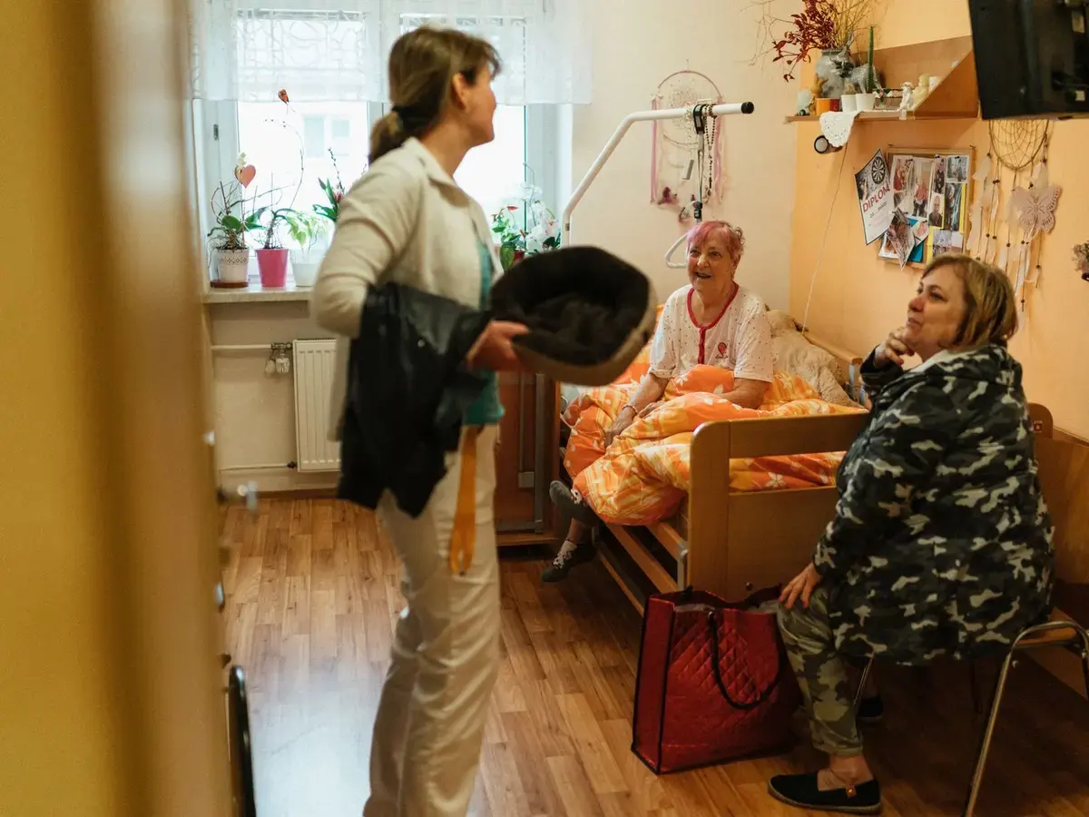 A caregiver talking with residents in a welcoming care-home room.