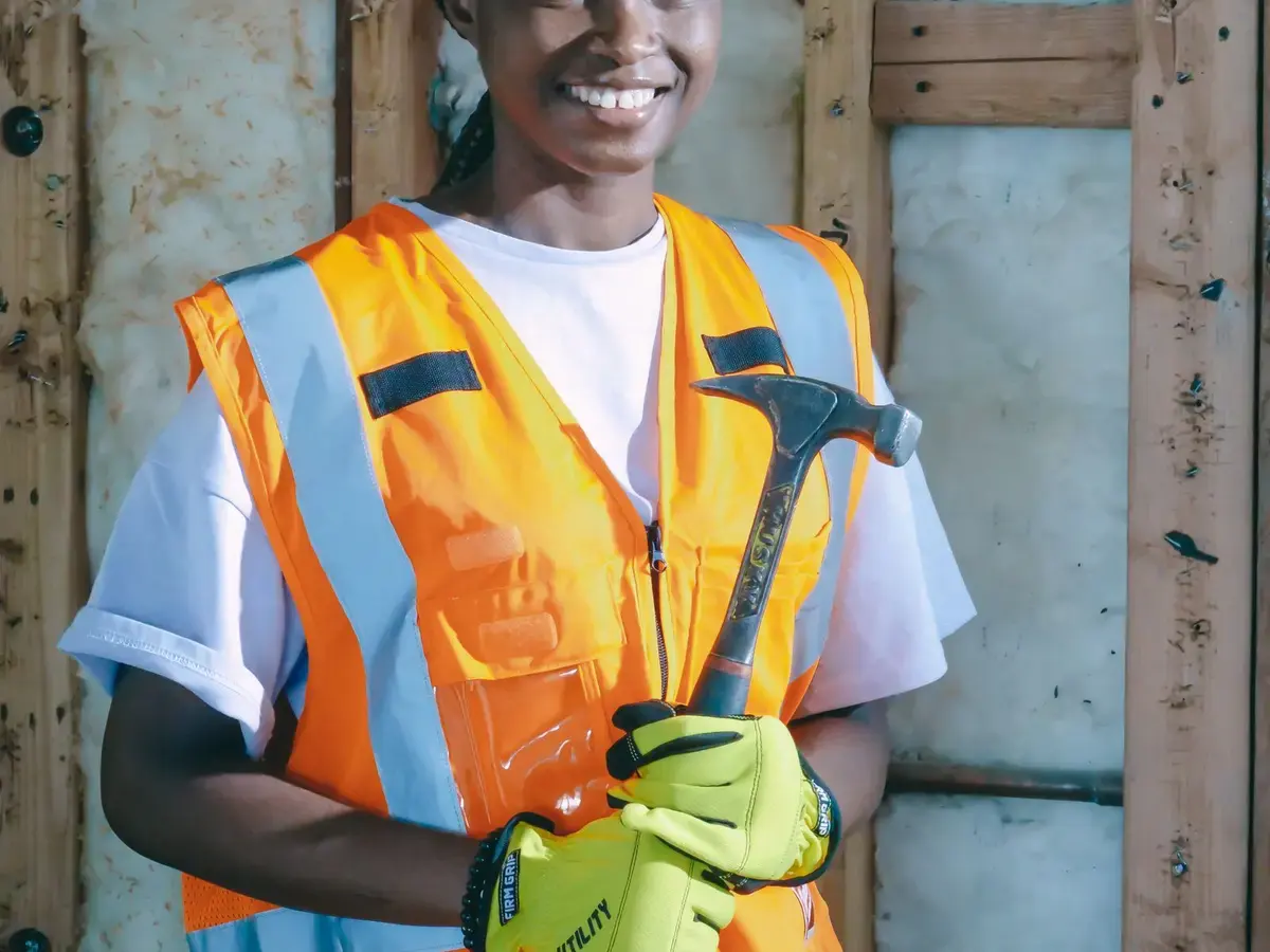 A smiling tradesperson holding a hammer indoors.